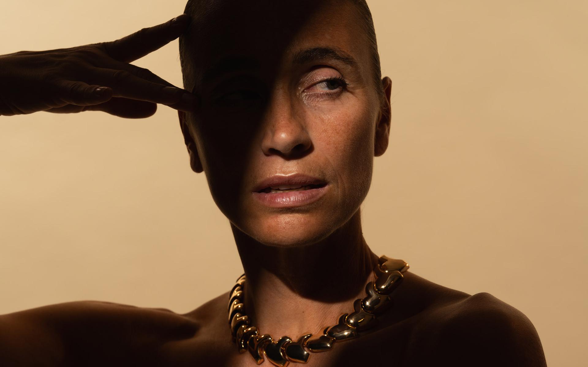 Frau mit kurzem Haar und goldener Kette, Hand an der Schläfe, Schatten im Gesicht