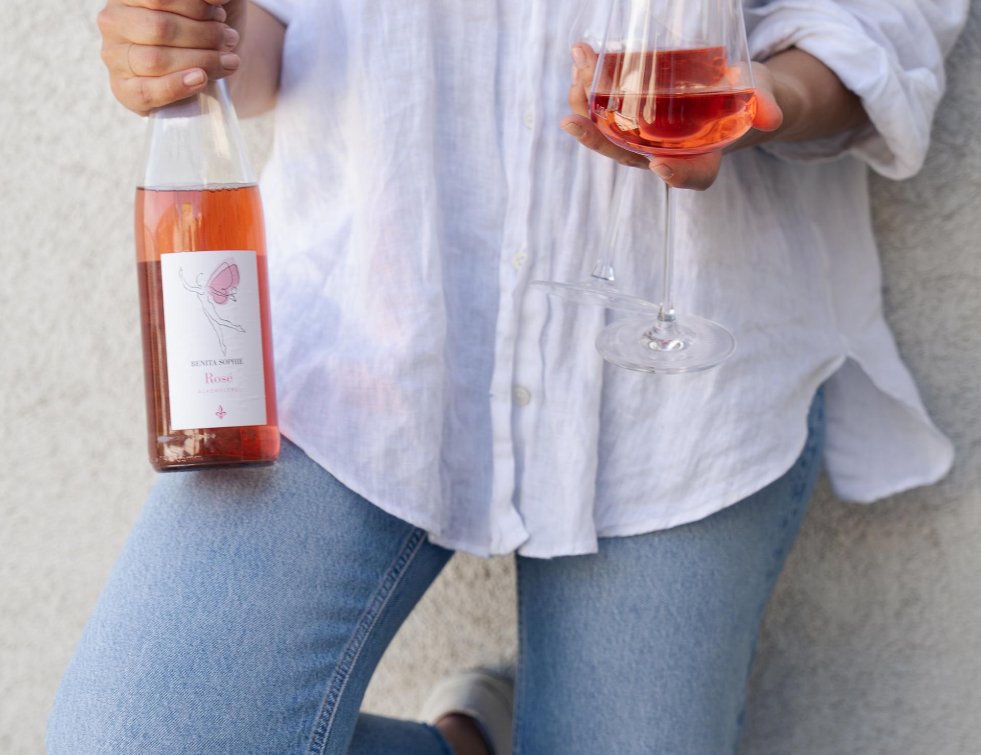Person hält eine Roséweinflasche und ein gefülltes Glas
