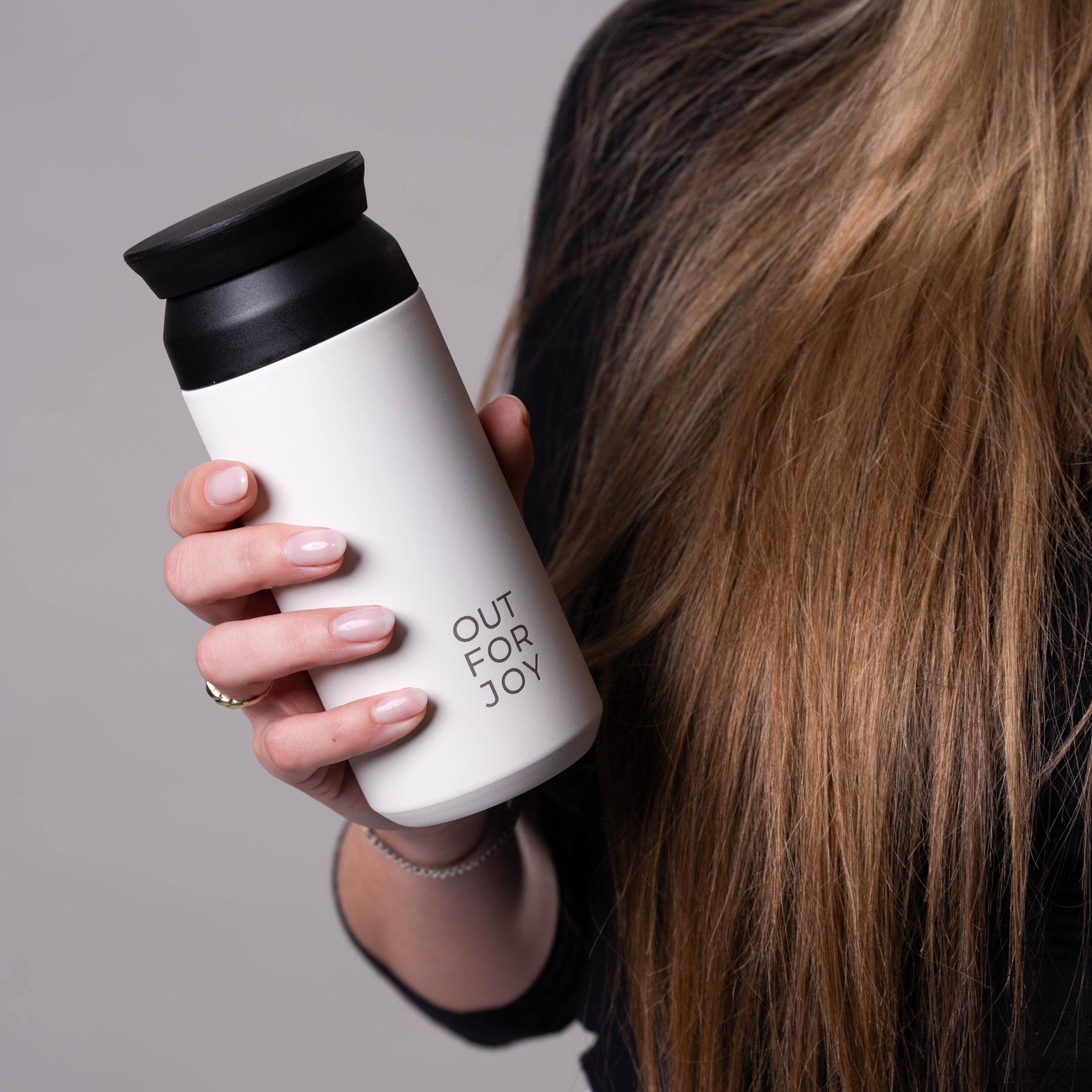 Hand hält eine weiße Out-For-Joy-Flasche vor langem Haar