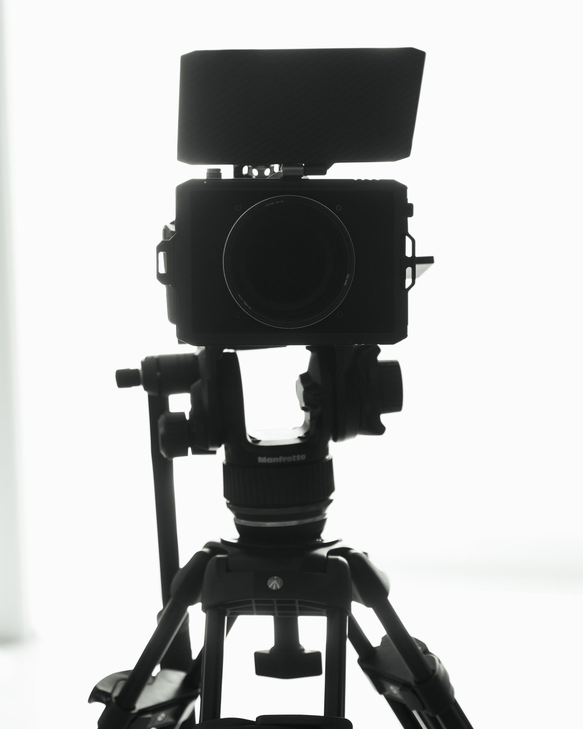 Videokamera auf einem Stativ im Gegenlicht vor hellem Hintergrund, schwarzweiß