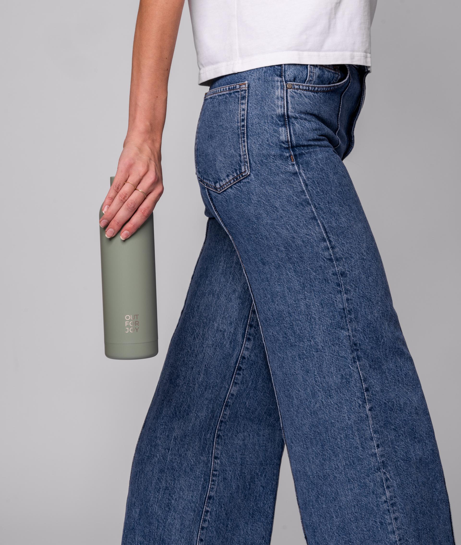 Hand hält eine olivgrüne Trinkflasche neben einer Jeans