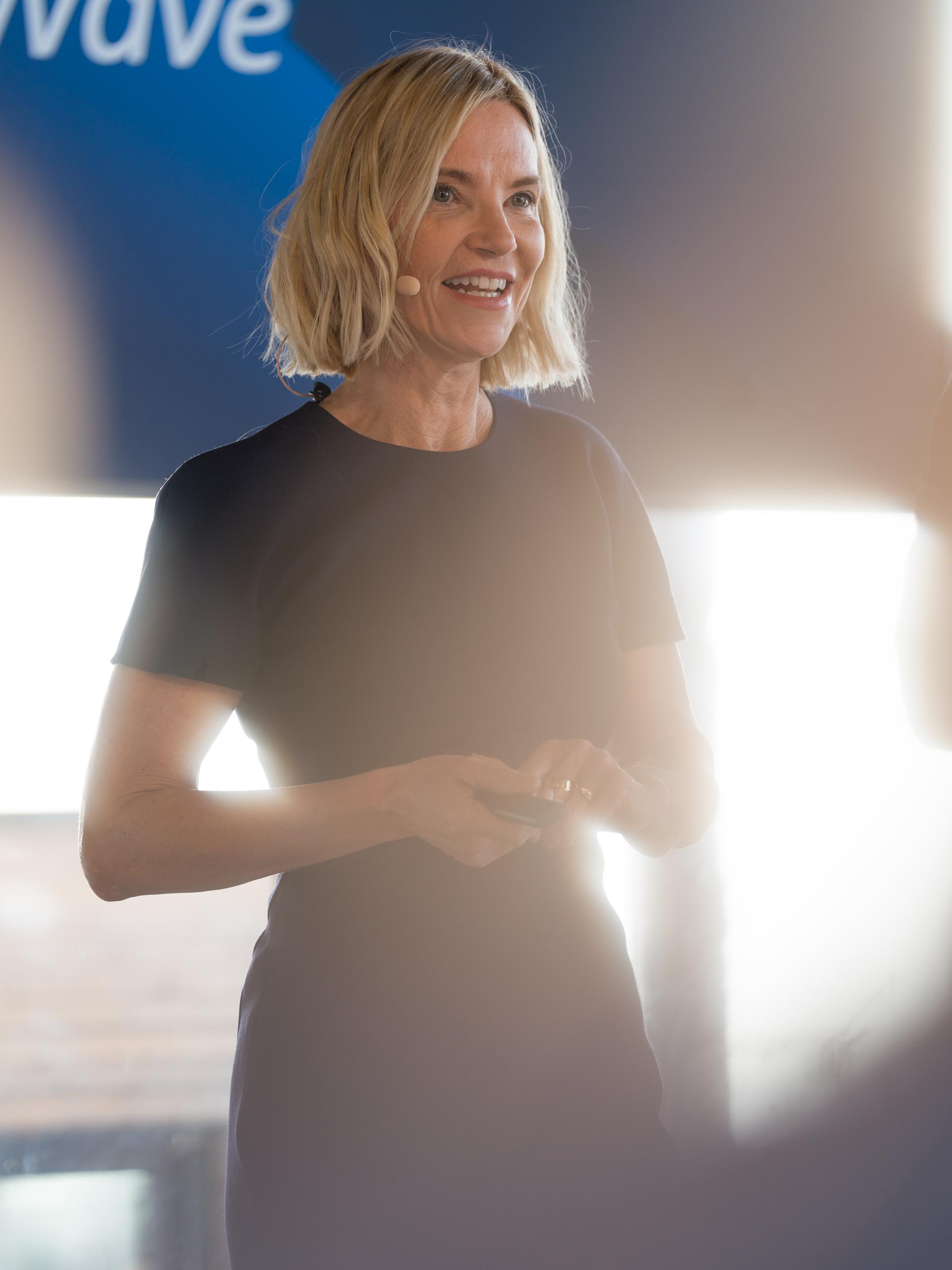 Blonde Referentin in dunklem Kleid spricht mit Headset bei einer Veranstaltung