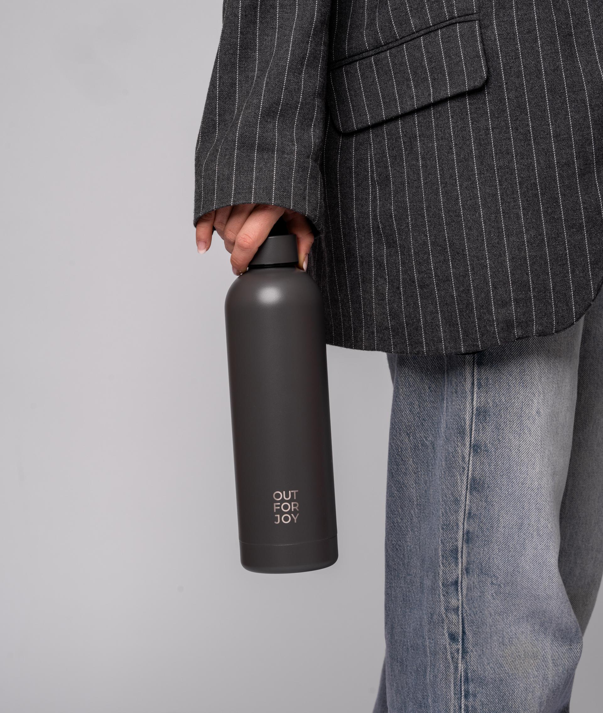 Hand hält eine graue Trinkflasche neben einem Nadelstreifensakko