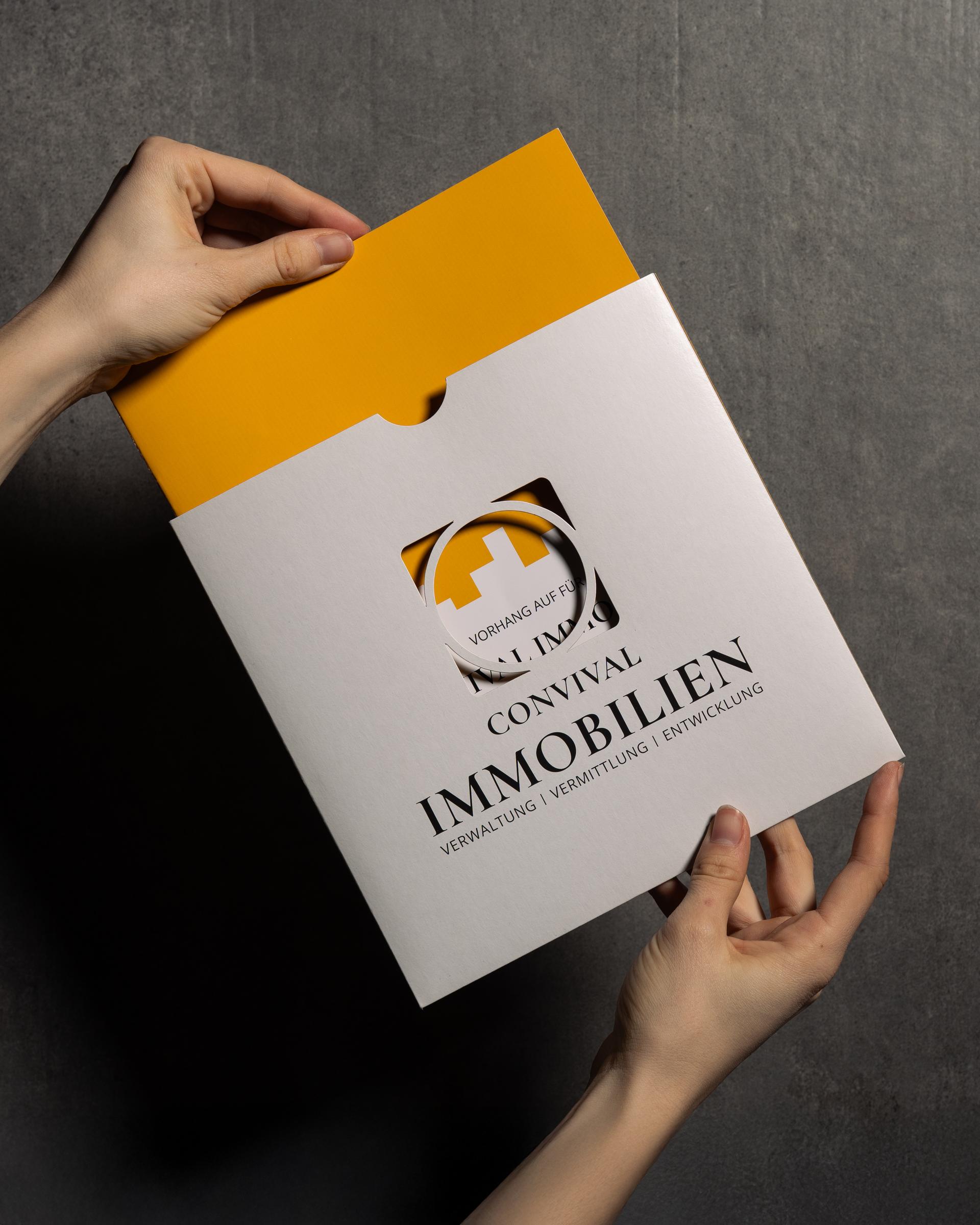 Hände halten eine Präsentationsmappe mit dem Logo von Convival Immobilien