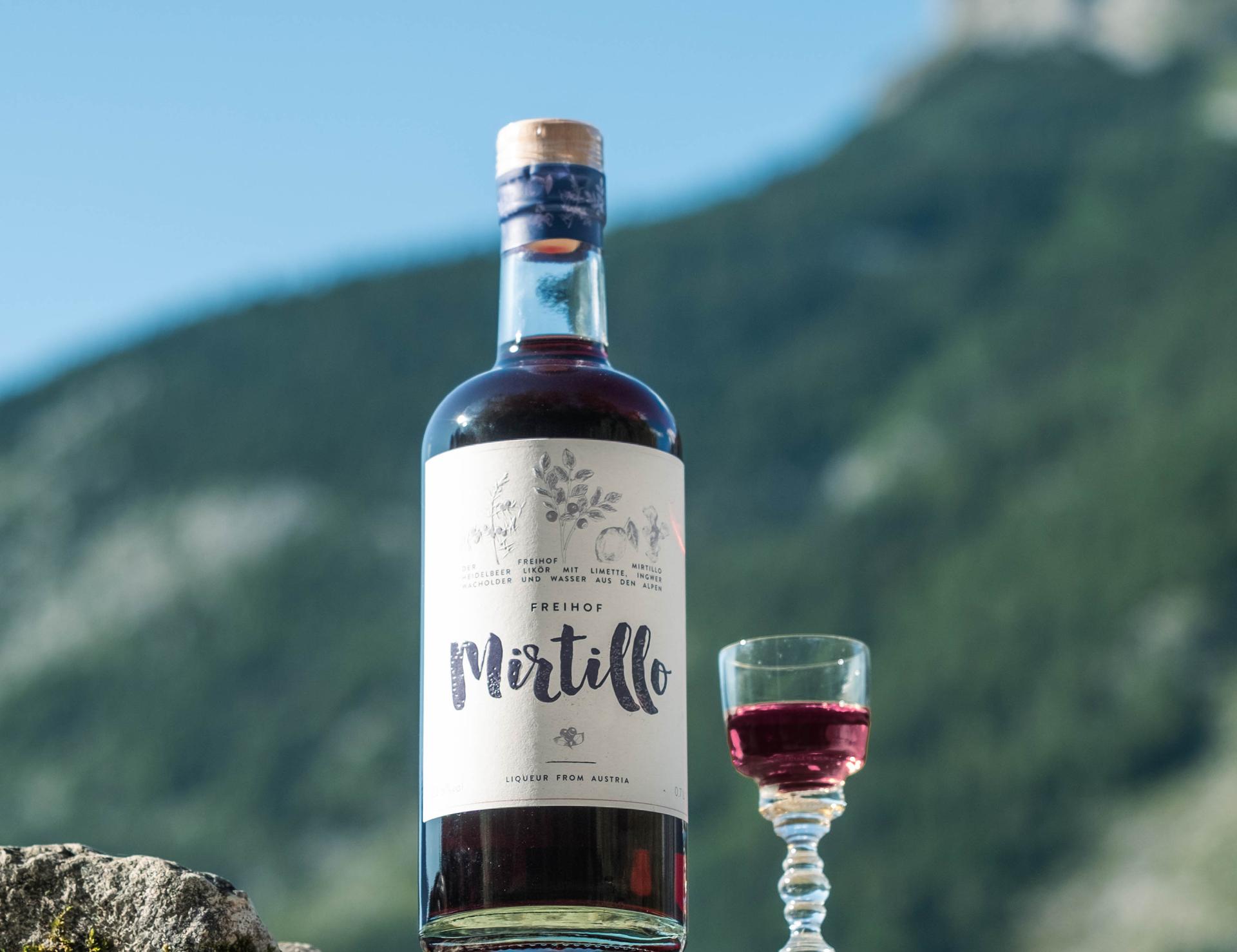 Flasche Mirtillo-Likör vor Berglandschaft mit gefülltem Glas