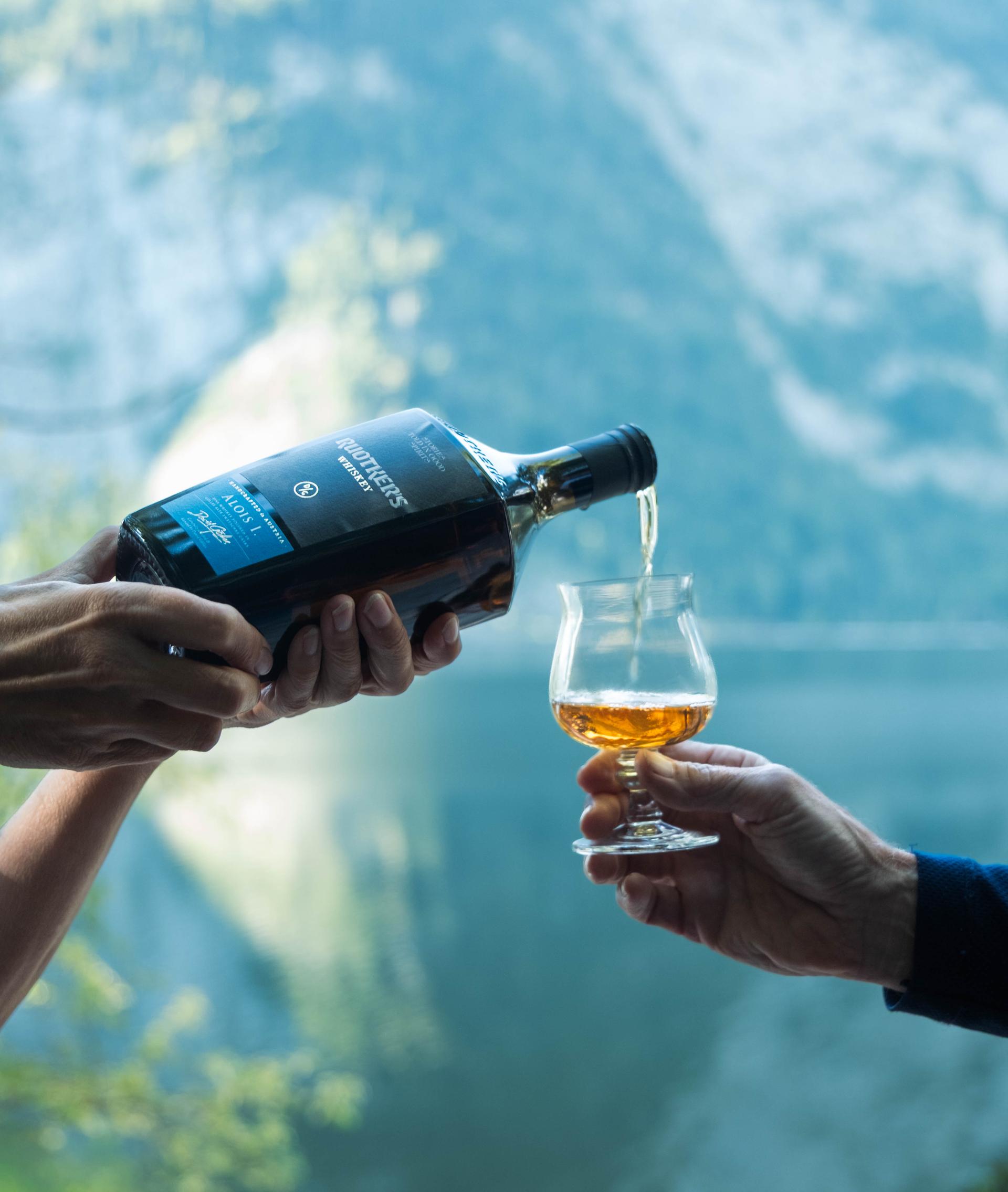 Hände gießen Whisky aus einer Flasche in ein Nosing-Glas