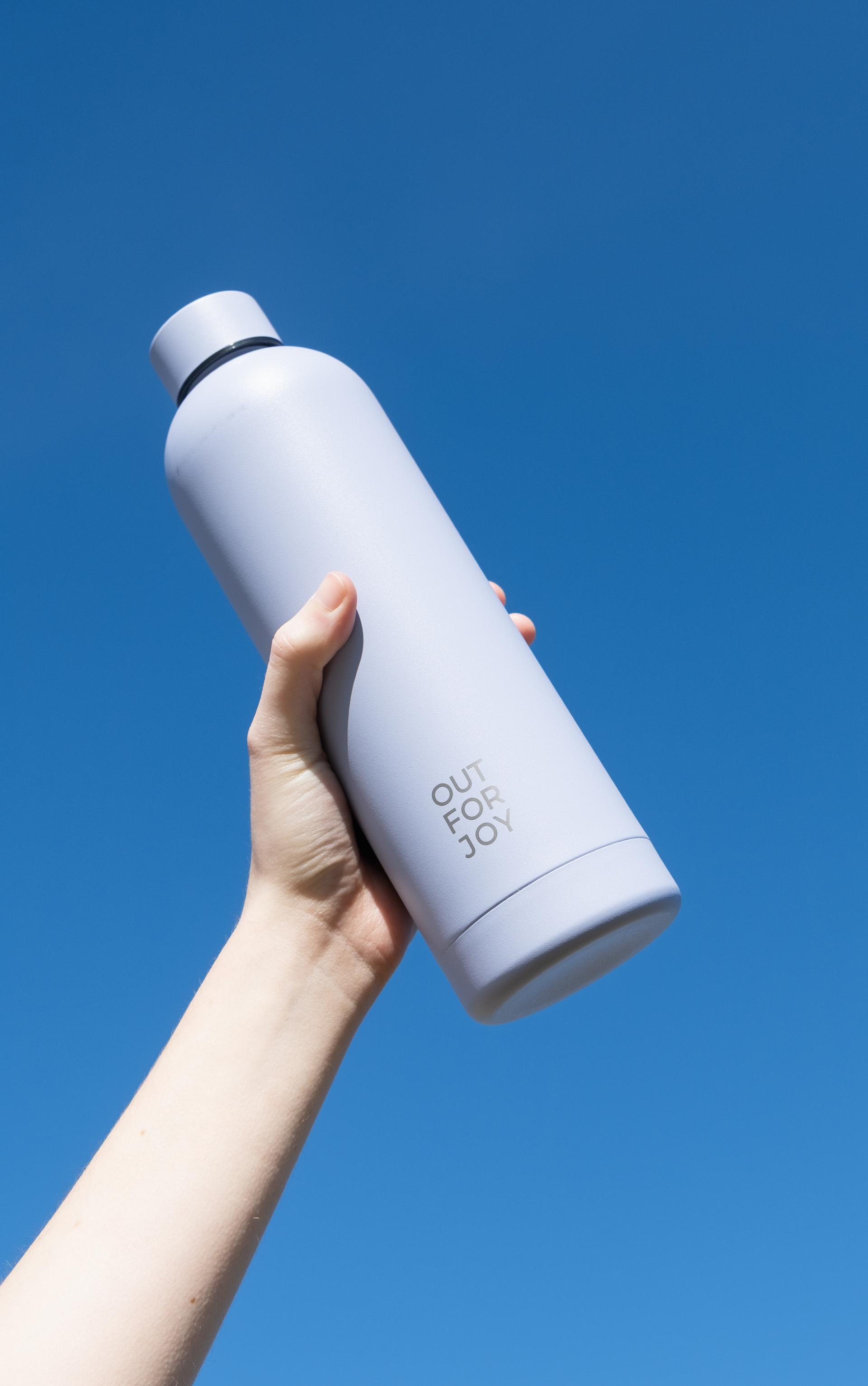 Hand hält eine weiße Out-For-Joy-Trinkflasche vor blauem Grund
