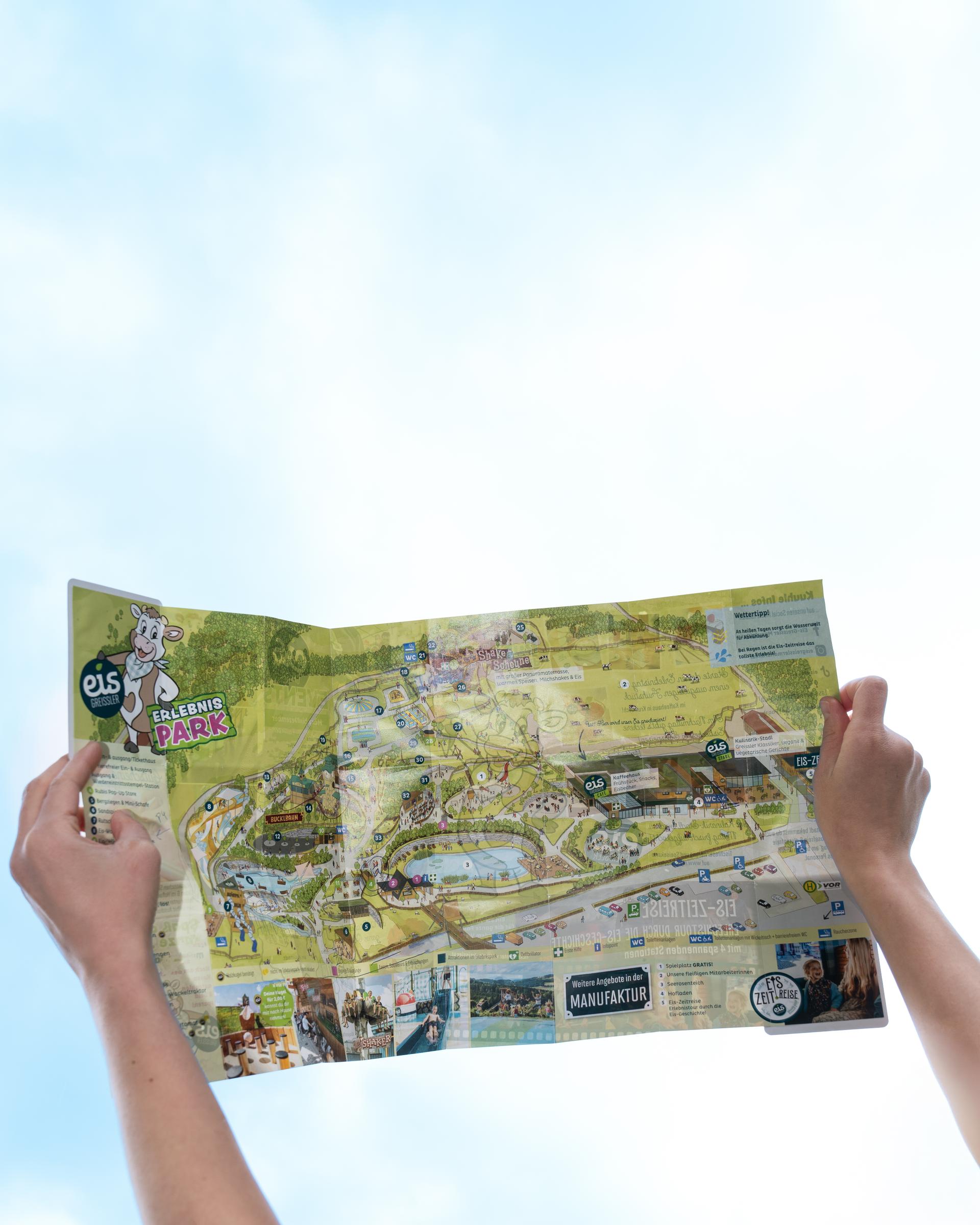 Hände halten einen aufgeklappten, illustrierten Parkplan