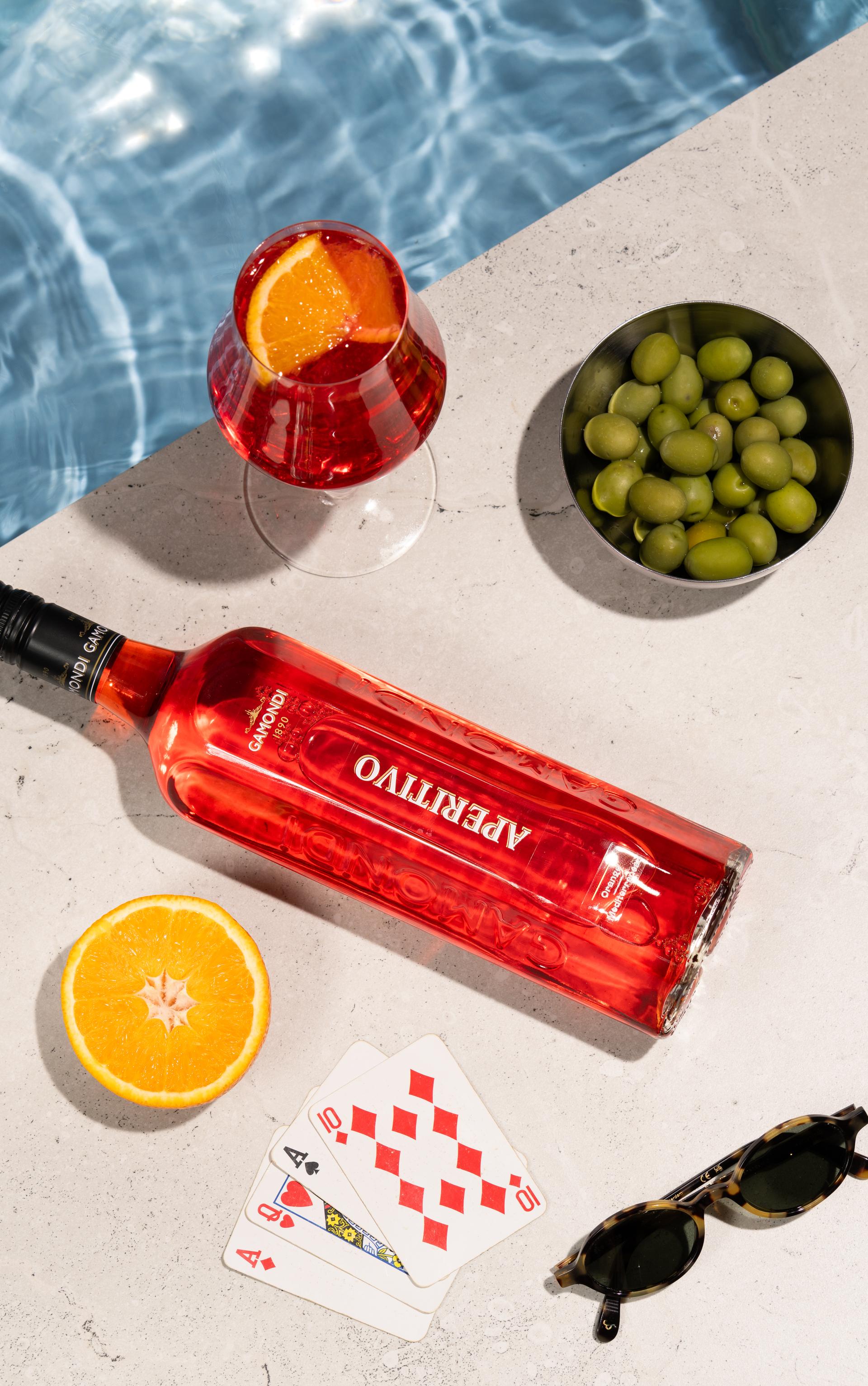Aperitivo-Flasche liegt neben Oliven und Orangenscheibe