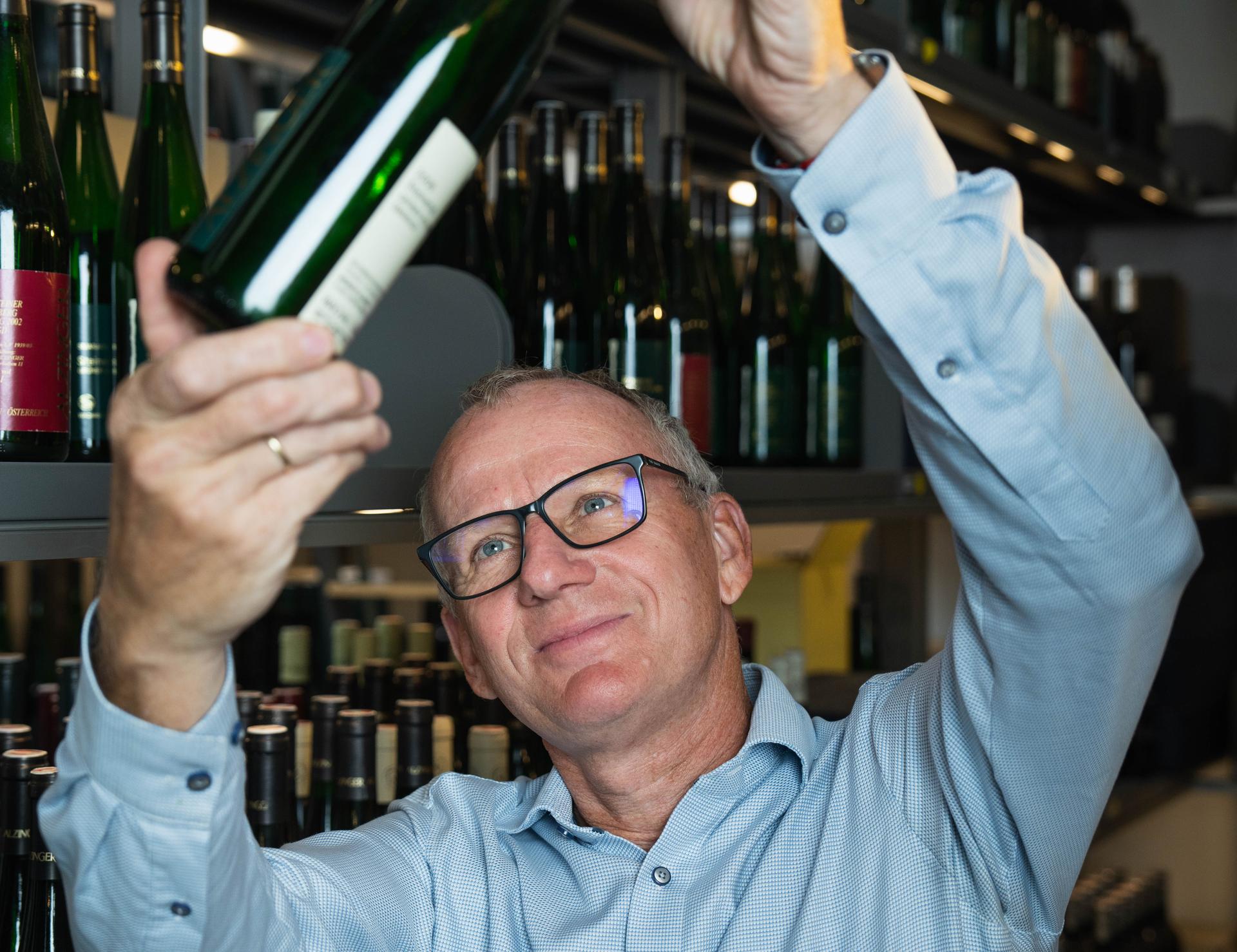 Mann mit Brille zieht eine Flasche aus einem Regal