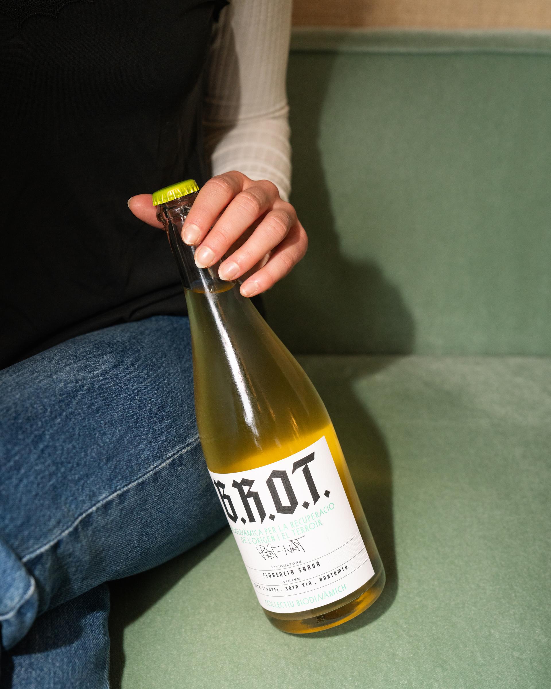 Hand öffnet eine Flasche Naturwein vor grüner Wand