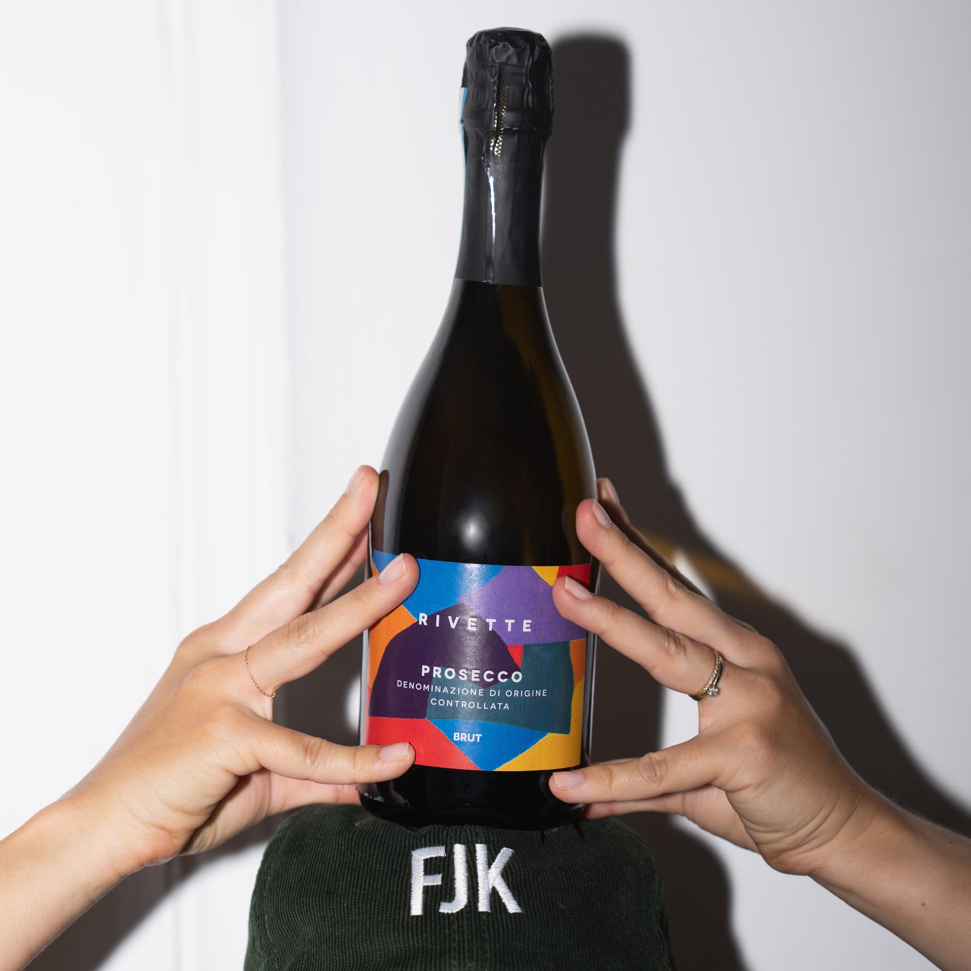 Hände halten eine Rivette-Prosecco-Flasche mit buntem Etikett