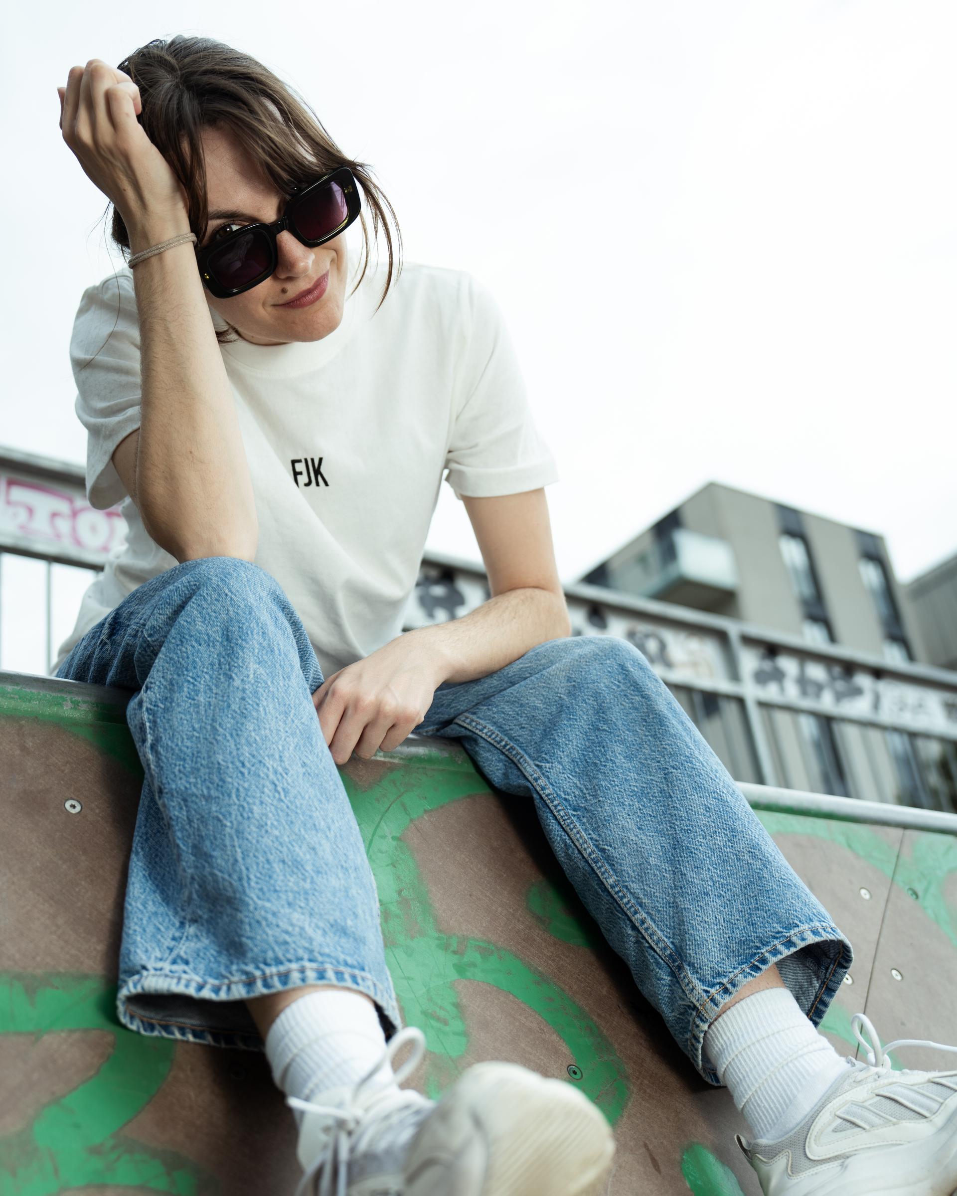 Person im weißen T-Shirt mit franzjohann-Print sitzt auf einer Betonkante
