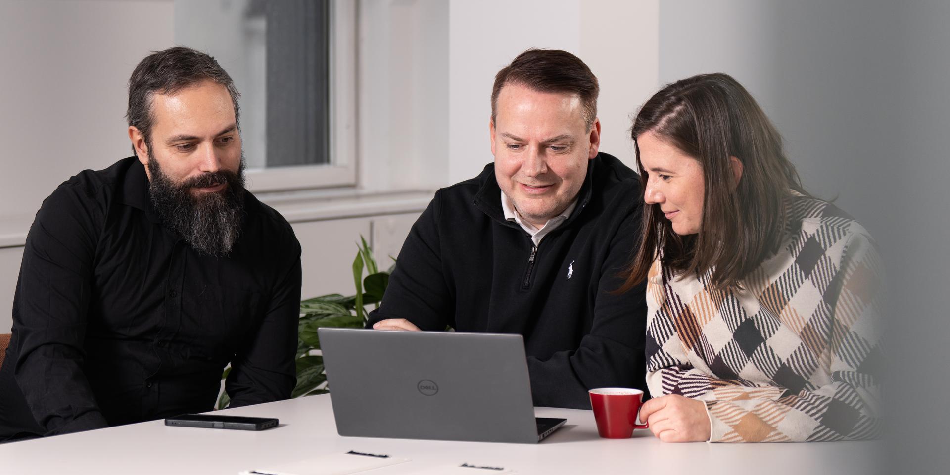 Drei Personen arbeiten gemeinsam an einem Laptop