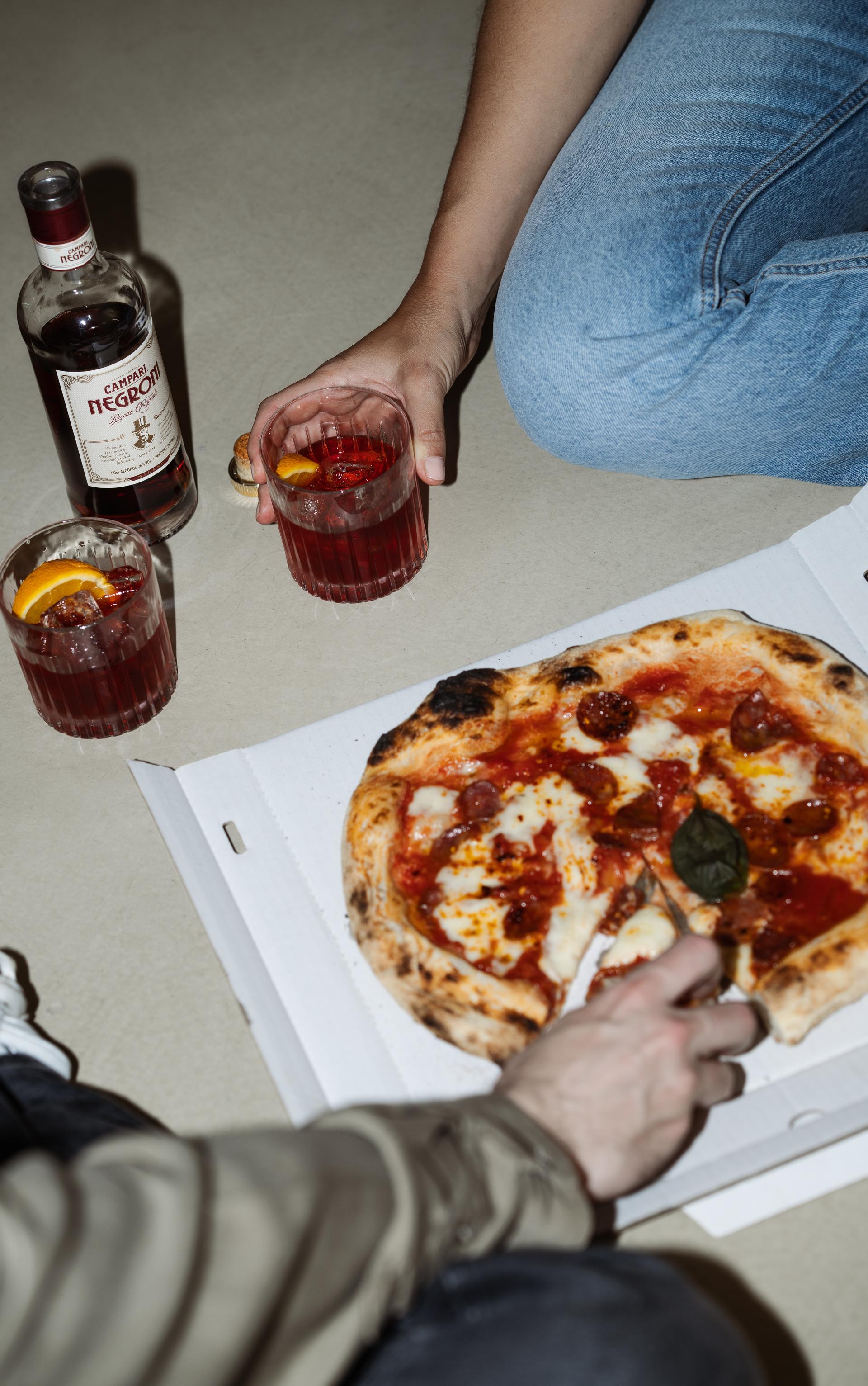 Blick von oben auf Pizza und zwei Negroni-Gläser