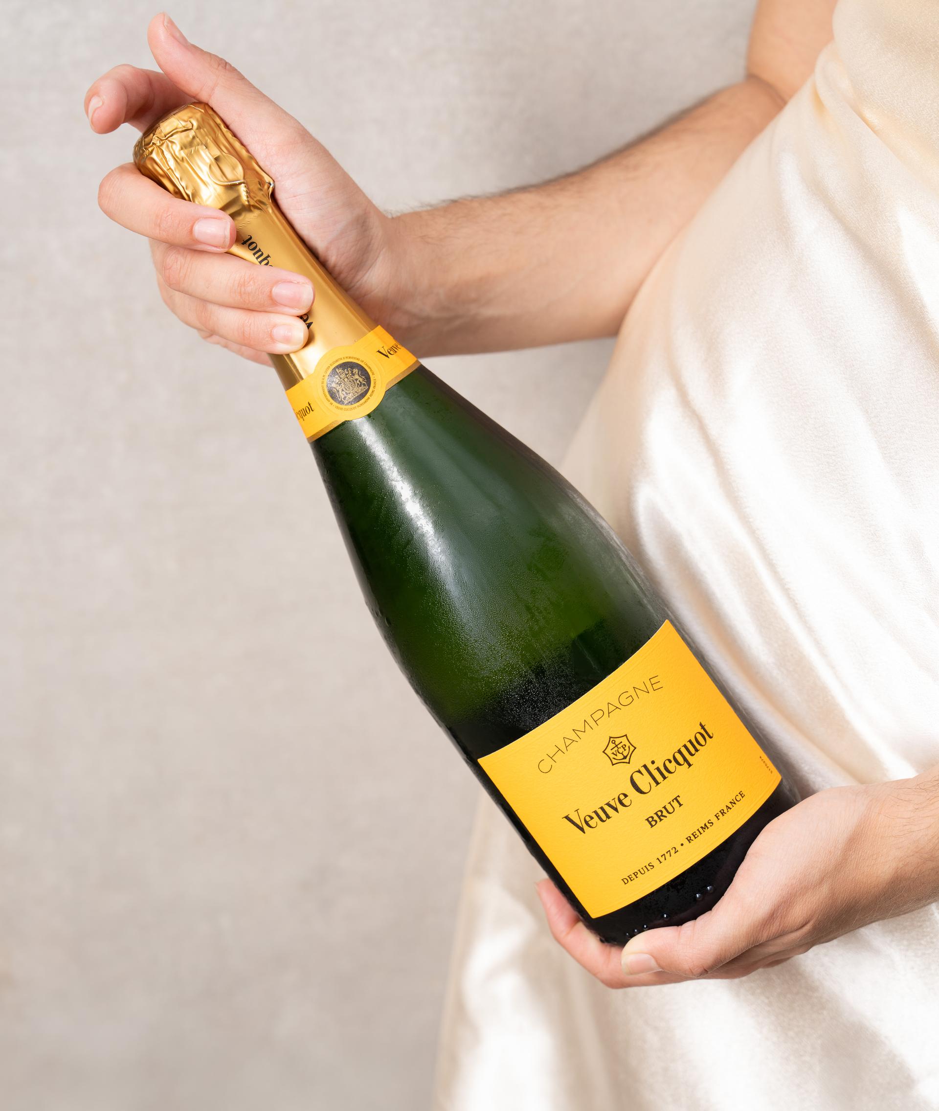 Hand hält eine Flasche Veuve Clicquot vor hellem Hintergrund