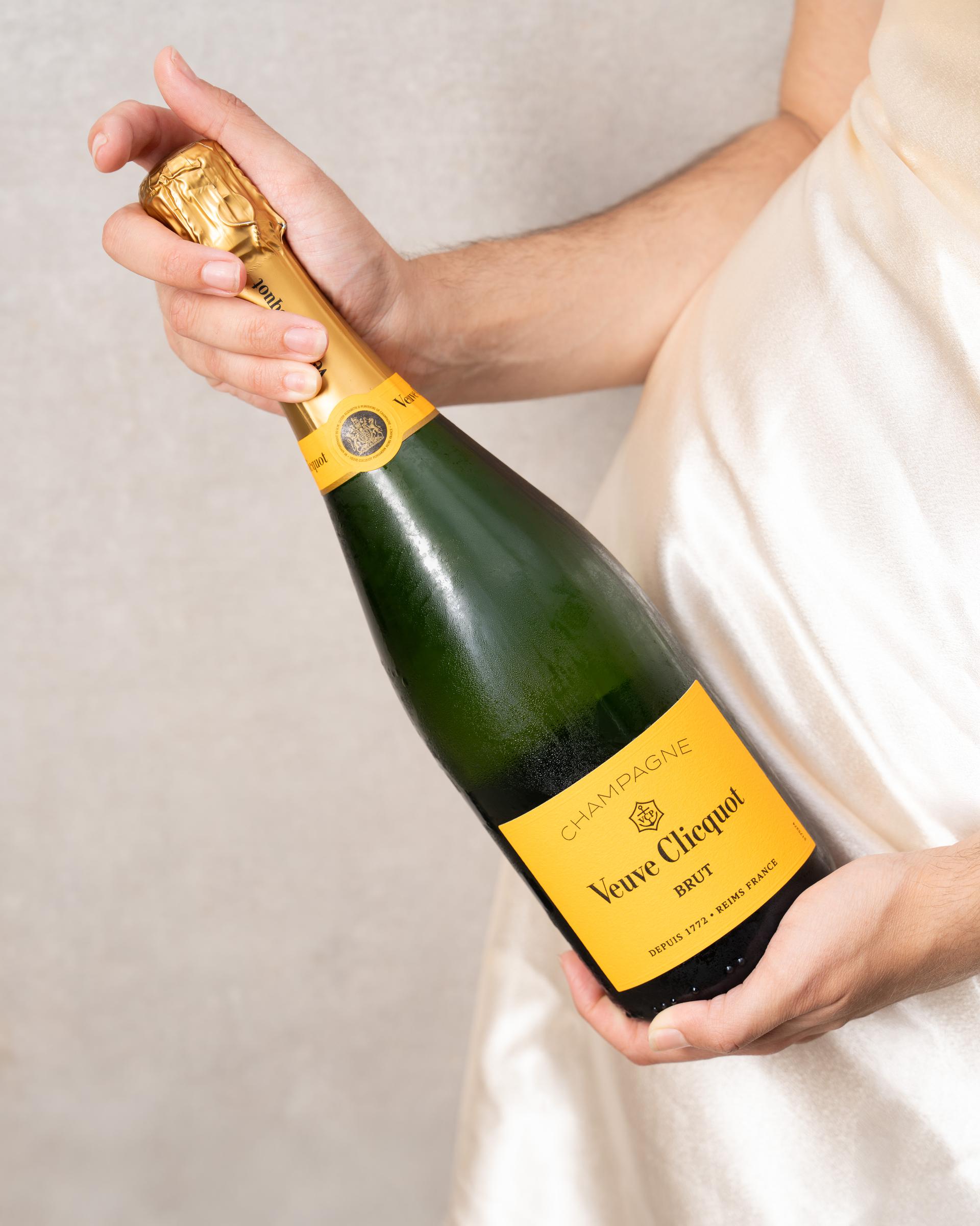 Hand hält eine Flasche Veuve Clicquot vor hellem Hintergrund