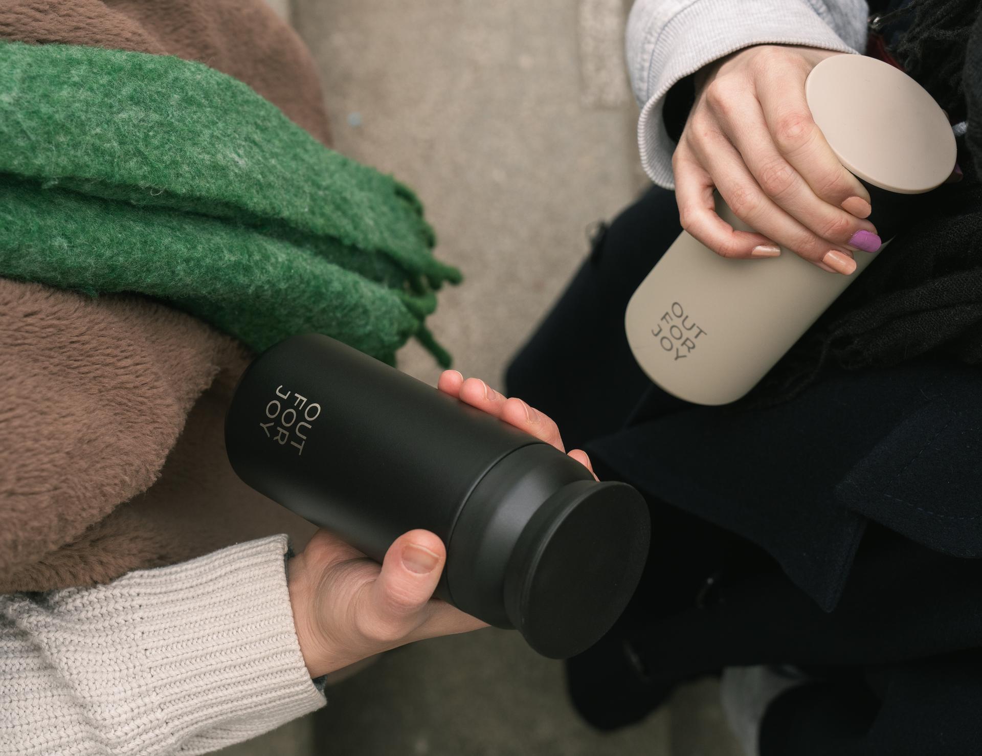 Zwei Hände halten eine schwarze und eine beige Trinkflasche