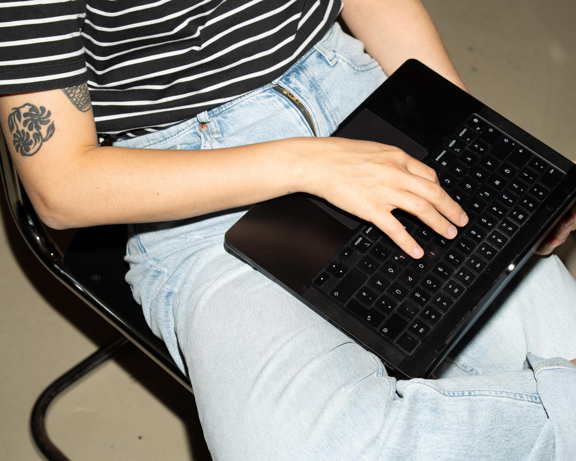 Person mit Tattoo tippt auf einer Tastatur auf dem Schoß