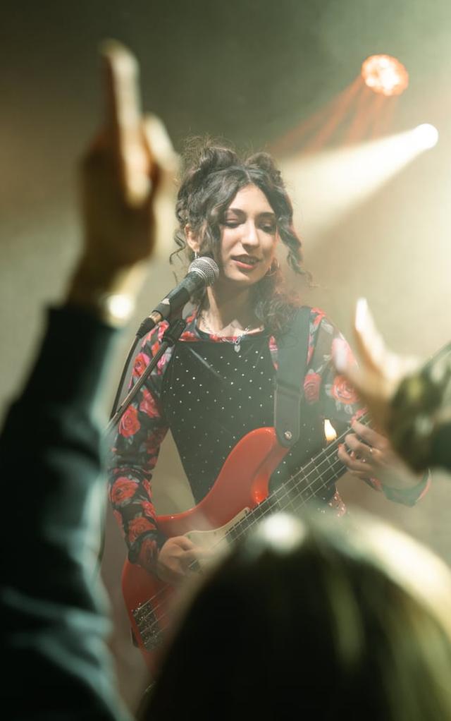 Ayla singt mit rotem Bass auf der Bühne, Hände des Publikums im Vordergrund