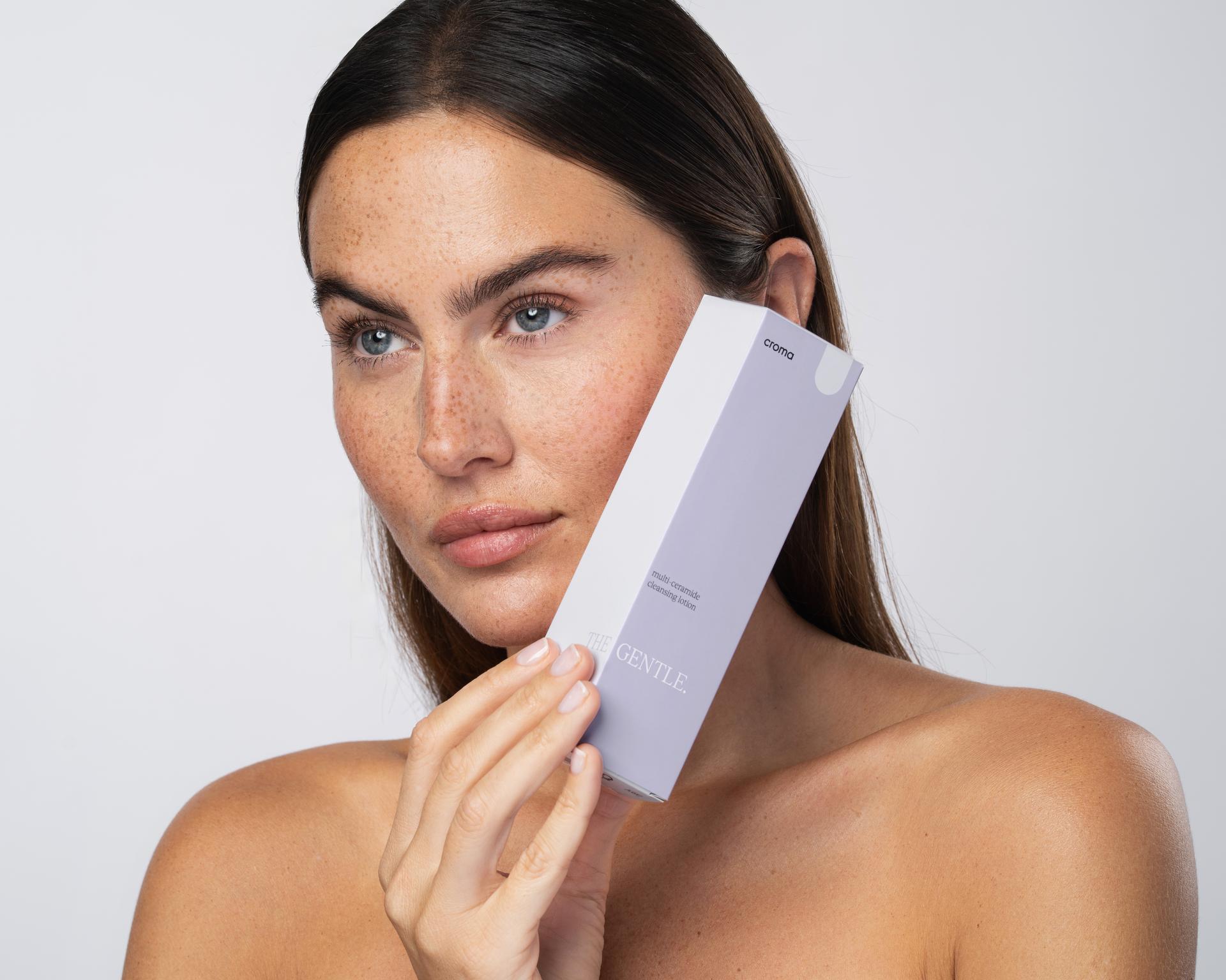 Frau mit Sommersprossen hält eine Croma-Gentle-Verpackung ans Gesicht