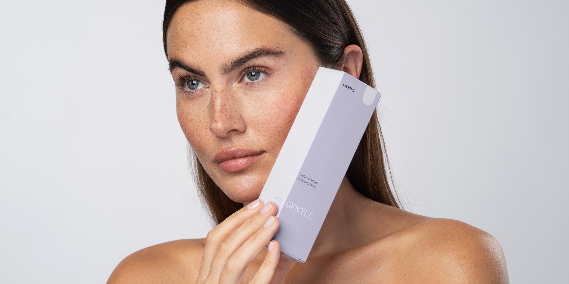 Frau mit Sommersprossen hält eine Croma-Gentle-Verpackung ans Gesicht