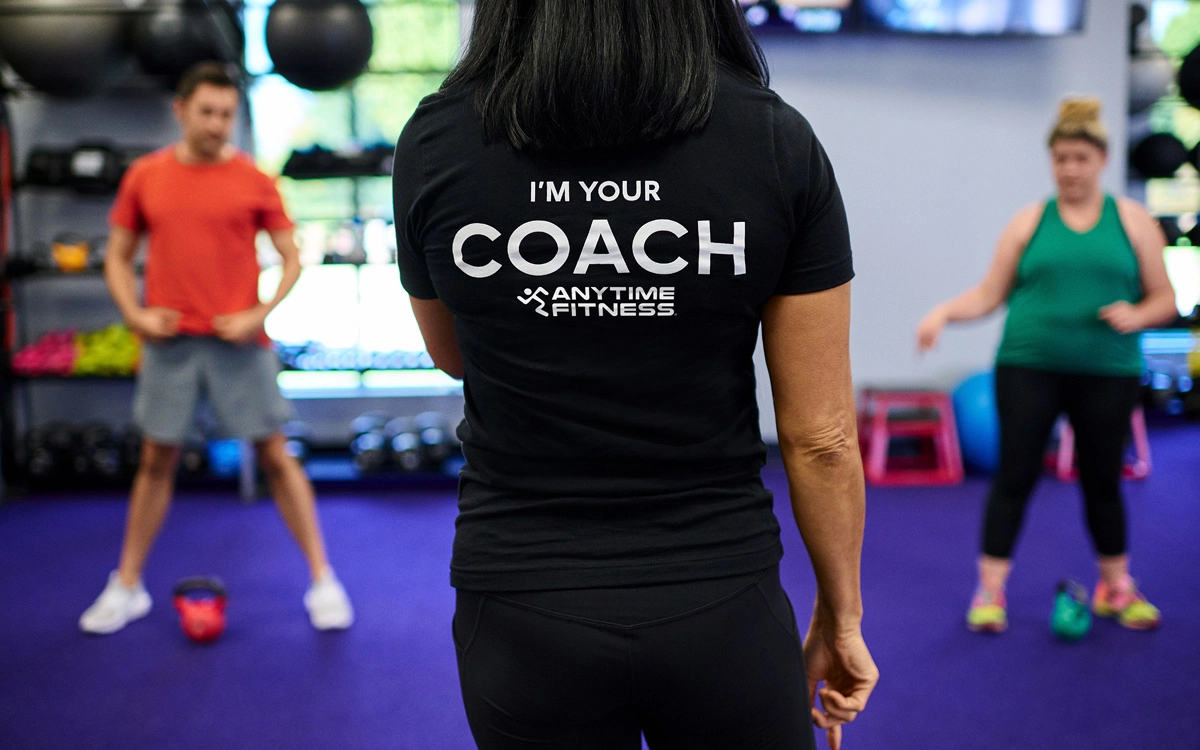 A trainer guides a smiling participant through a workout in a group fitness class