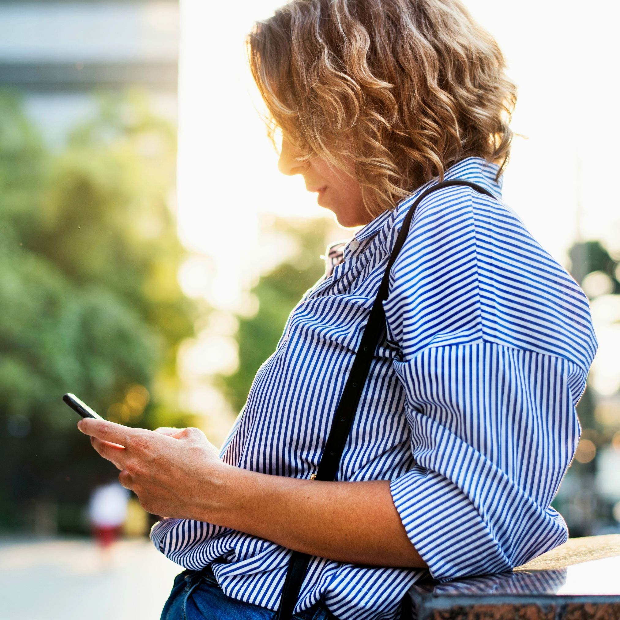 A woman standing outdoors, looking at her phone.
