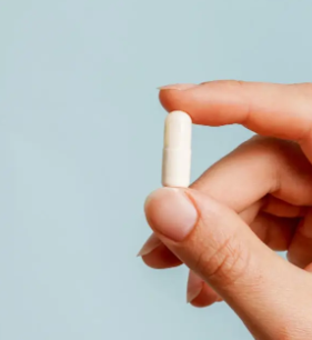 A single white tablet resting in an open hand against a blue background.