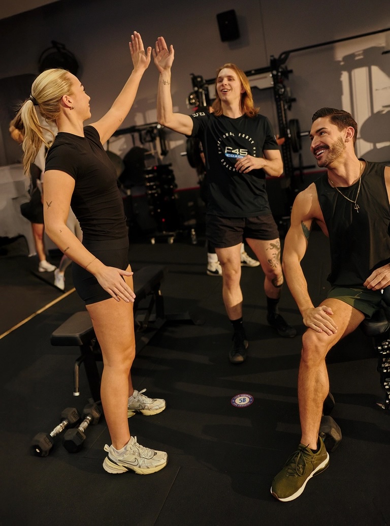 Three people in a gym celebrate with a high-five during a workout.