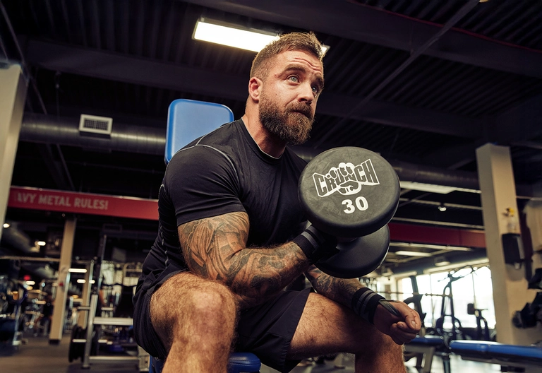 Man performing a seated dumbbell curl at a gym.