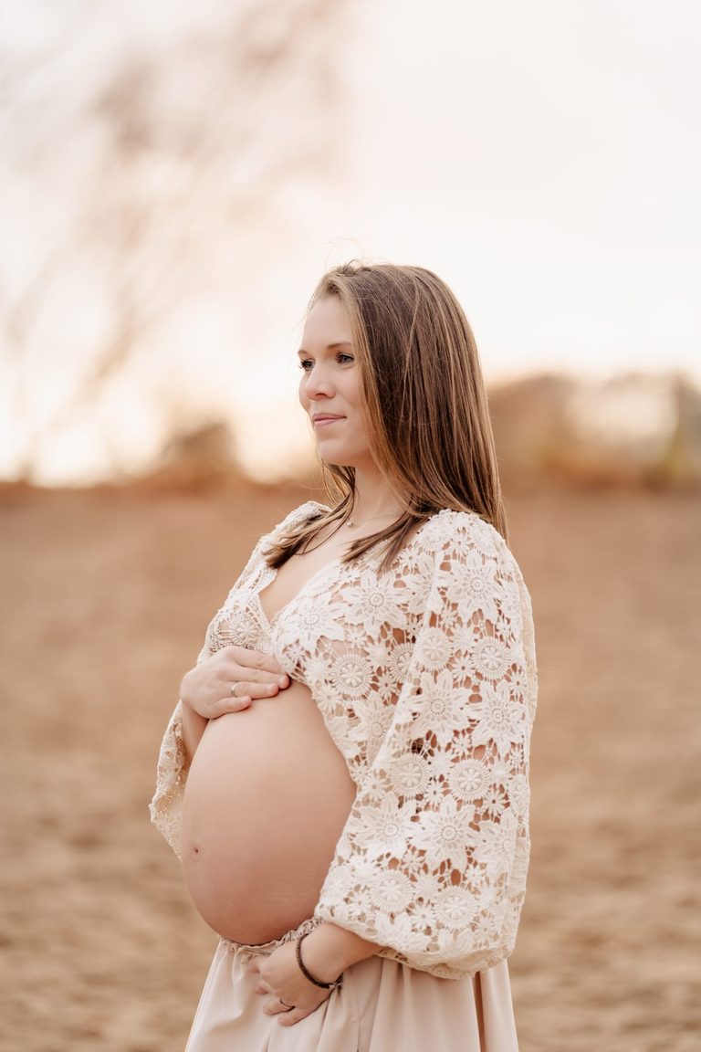 Babybauch im Spitzenkleid im warmen Licht