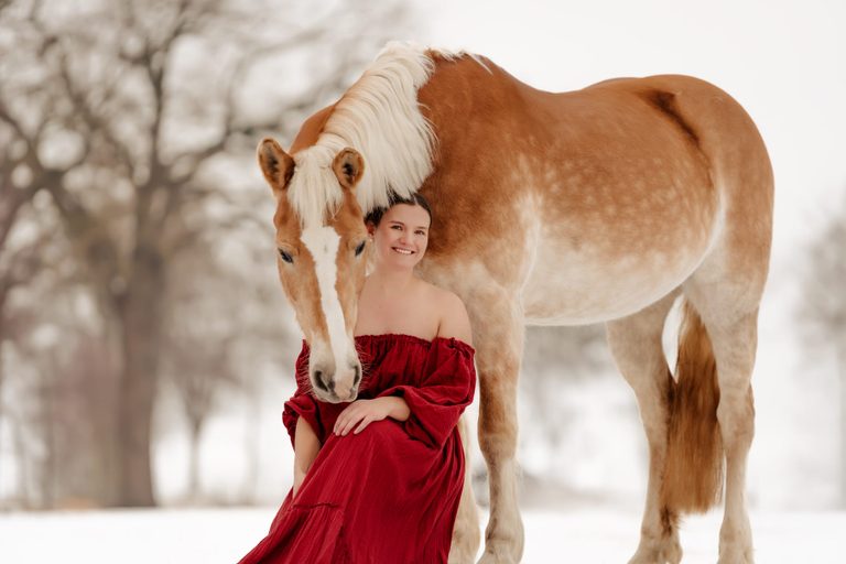 Frau in rotem Kleid mit Haflinger im Schnee