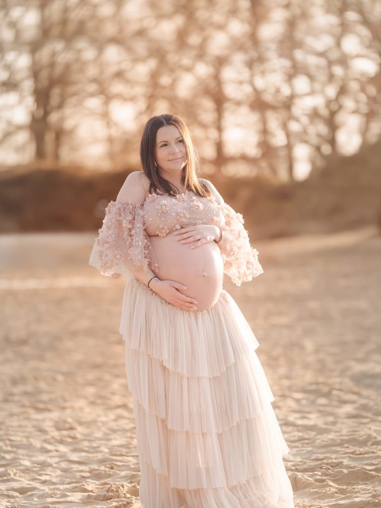 Schwangere im Tüllkleid am Wasser im Sonnenuntergang