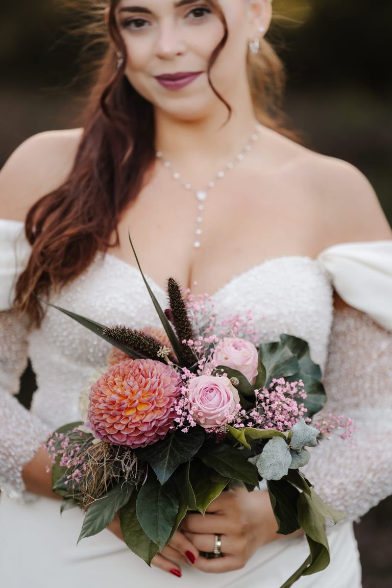 Braut hält ihren Brautstrauß aus Rosen, Dahlie und Eukalyptus in den Händen