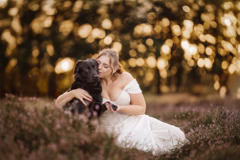 Braut im Brautkleid schmiegt sich an ihren großen schwarzen Hund