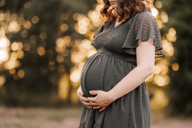 Babybauch im dunkelgrünen Kleid im Abendlicht