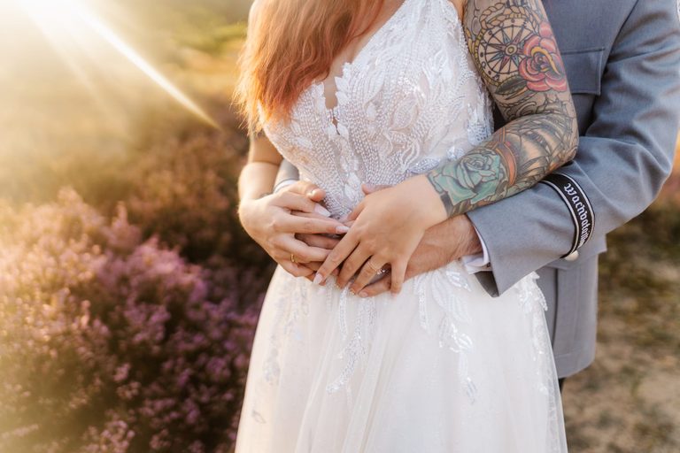 Hände des Brautpaars mit Eheringen auf dem Brautkleid im warmen Abendlicht