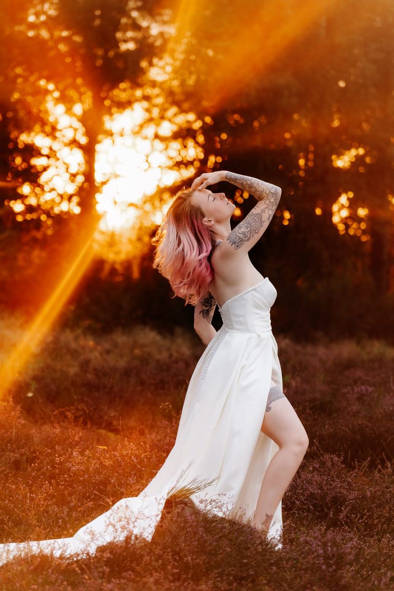 Braut tanzt im Brautkleid durch die Heide, Sonnenstrahlen im Gegenlicht