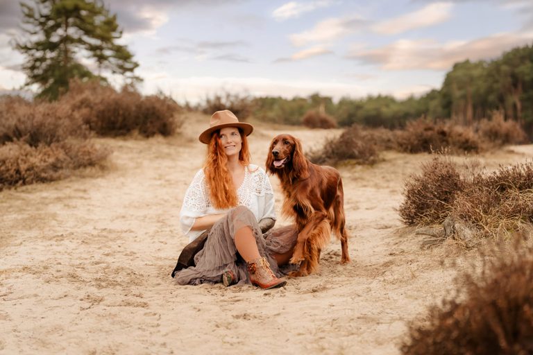 Frau sitzt mit Irish Setter im Sand