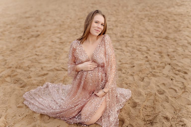 Schwangere im glitzernden Kleid am Sandstrand