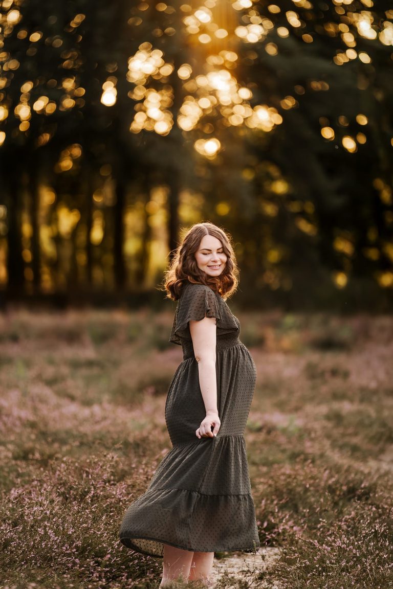 Schwangere dreht sich im grünen Kleid durch die Heide