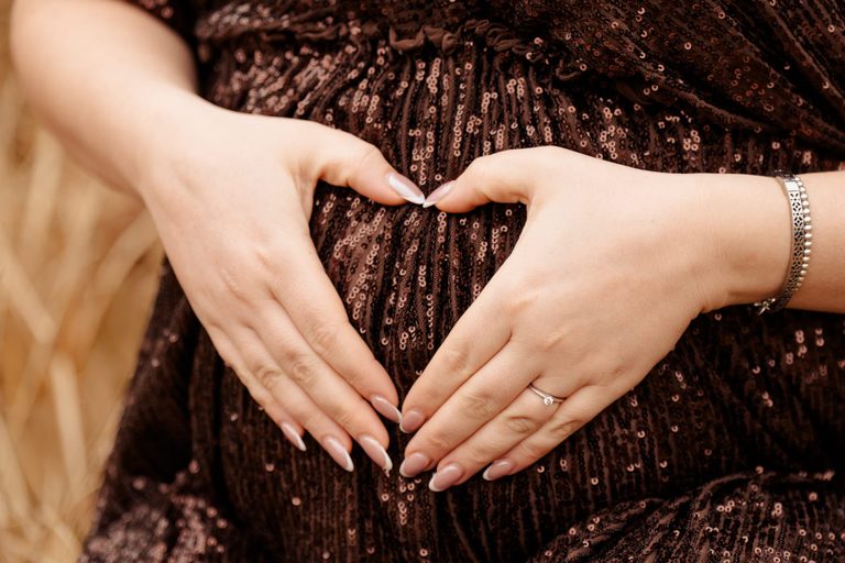 Hände formen ein Herz auf dem Babybauch