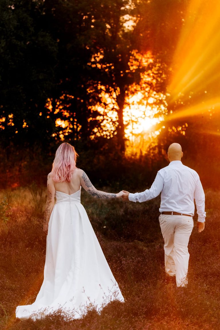 Brautpaar geht Hand in Hand durch die Heide der Abendsonne entgegen