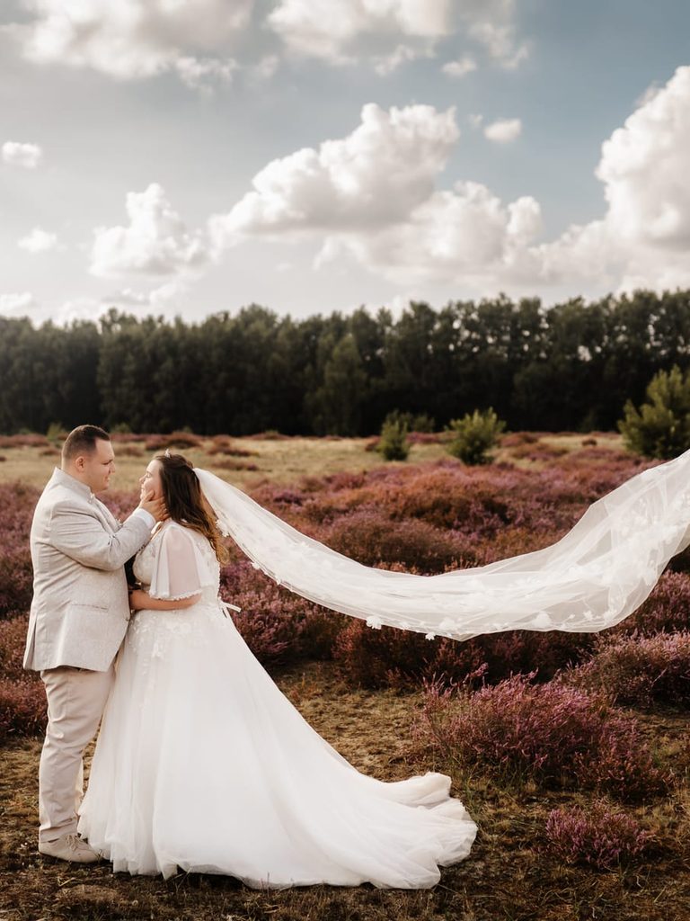 Brautpaar in der blühenden Heide, der Schleier weht im Wind