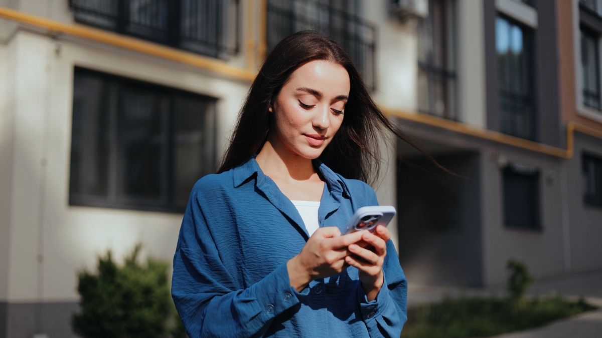 Woman in a blue shirt using her phone on a sunlit residential street