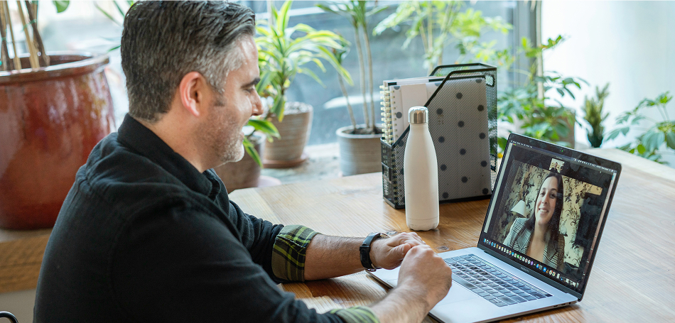 A man smiling during a video call with a woman visible on his laptop screen.