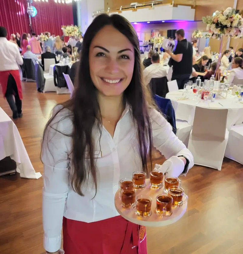 Serviceperson bietet Aperitif-Gläser an einem festlich gedeckten Hochzeitsanlass an
