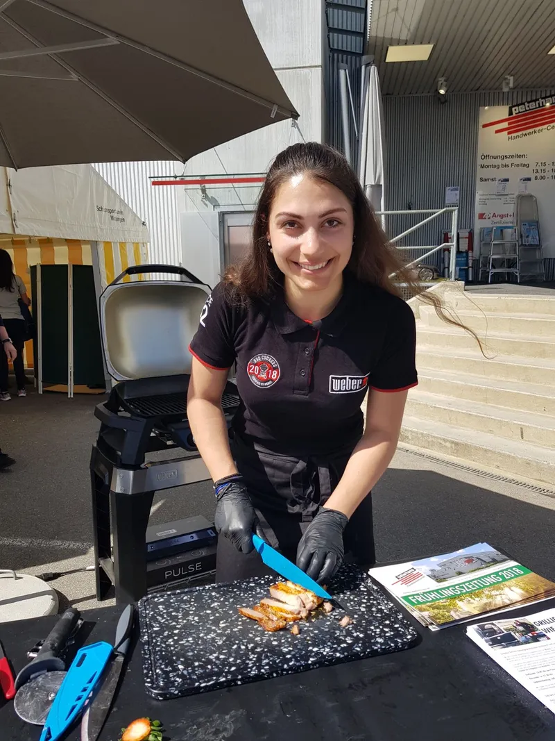 NNBS-Mitarbeiterin schneidet gegrilltes Fleisch an einem Weber-Stand