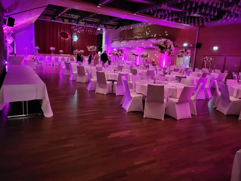 Festlich eingedeckter Ballsaal mit weiss bezogenen Stühlen und Blumendekoration